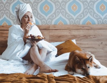 A girl with a towel on her head and a dog on the bed eats fruit for breakfast. Treat yourself